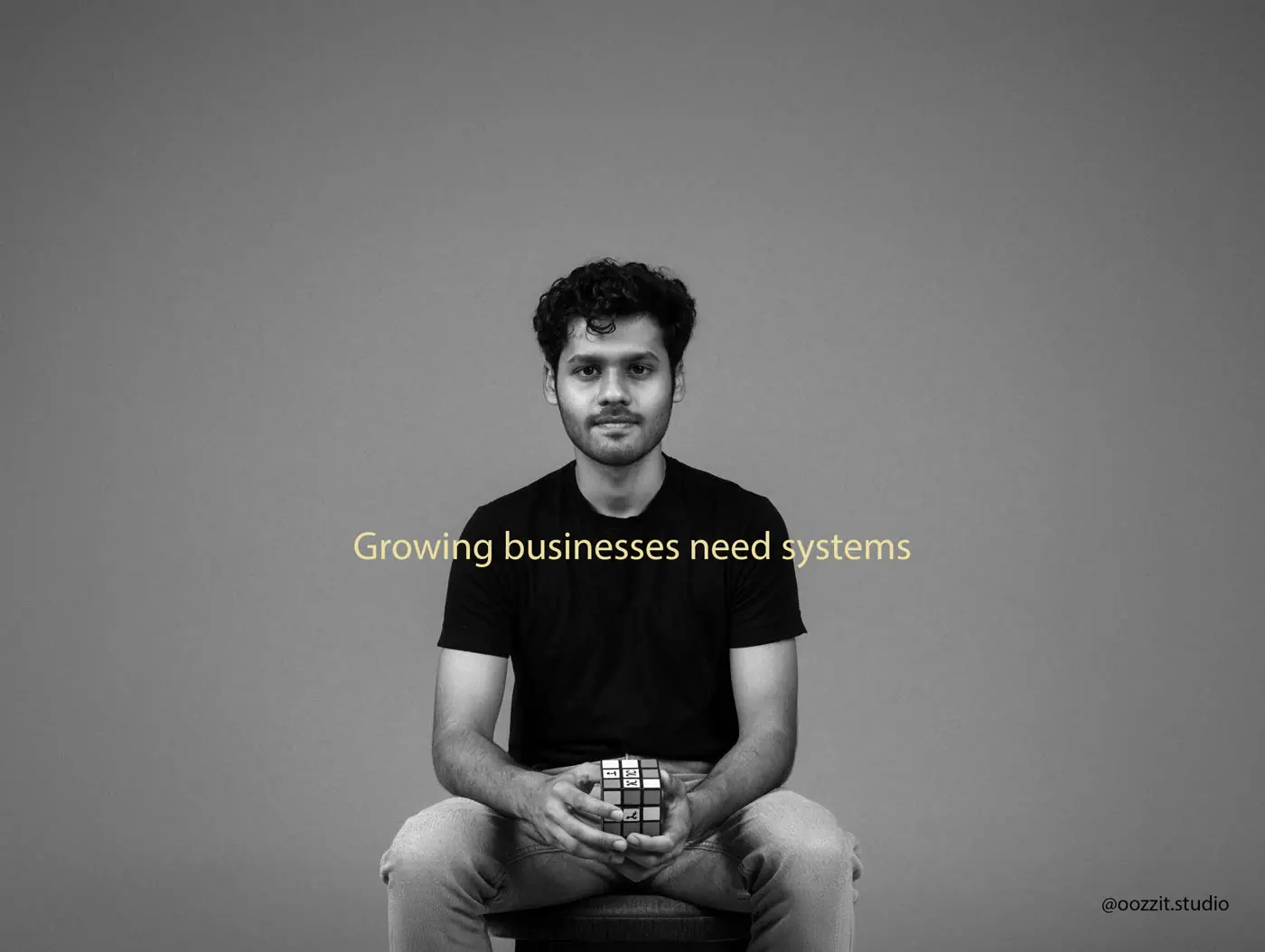 Aditya Shanker, seated, holding a puzzle cube, with the line Growing businesses need systems.