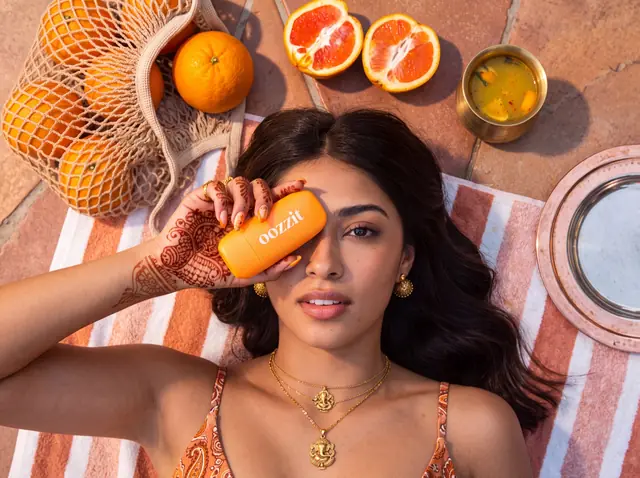 Concept campaign for suncare: a woman lies on a striped towel among oranges, holding an Oozzit tube over one eye.